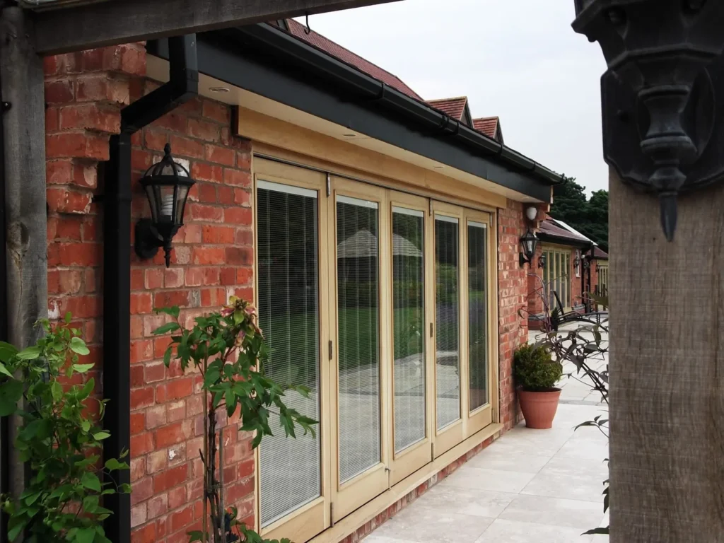 Wide set of timber sliding folding doors with integrated blinds, set in a red brick extension with patio, showcasing smooth movement and elegant design powered by Centor hardware.