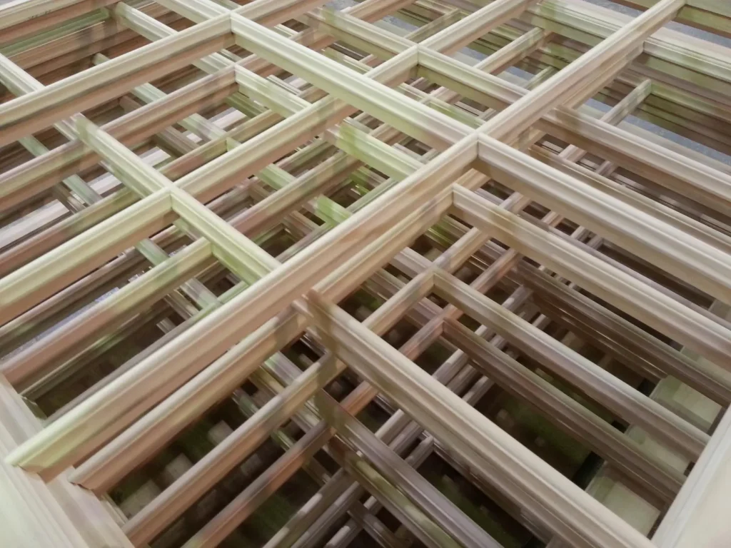 Close-up of finely crafted Accoya timber glazing bars stacked in a workshop. The image showcases the precision joinery and uniform grain of the modified wood, used in the manufacture of high-performance heritage-style windows.