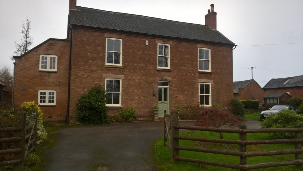 Front view of a renovated red brick farmhouse in Kirk Langley featuring Gowercroft Joinery’s white-painted Chatsworth sliding sash windows with Georgian astragal bars.