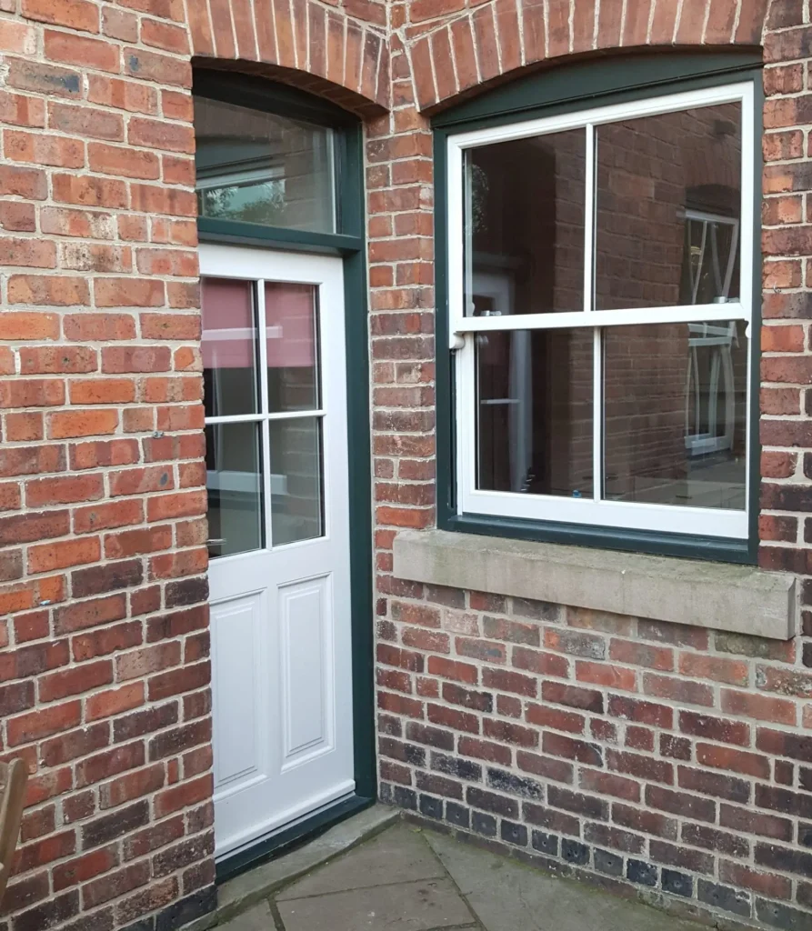 Close-up of a white timber sash window and a matching white timber door with a glazed panel, both set in a red brick wall with stone and arched brick details, demonstrating minimal wear after years of use.