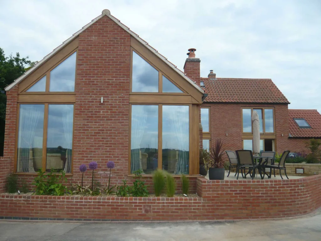 A beautifully designed red-brick country home in Newark featuring bespoke timber-framed windows that follow the building’s striking gable-end shape. The expansive glazing allows for panoramic countryside views while enhancing the home’s traditional charm. This property exemplifies Gowercroft’s ability to craft high-performance, custom-made timber windows that perfectly complement both classic and contemporary architectural styles.