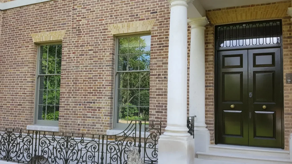 Heritage property featuring large timber sliding sash windows with narrow glazing bars and a traditional six-panel front door, showcasing the aesthetic compatibility of vacuum glazing in conservation settings.