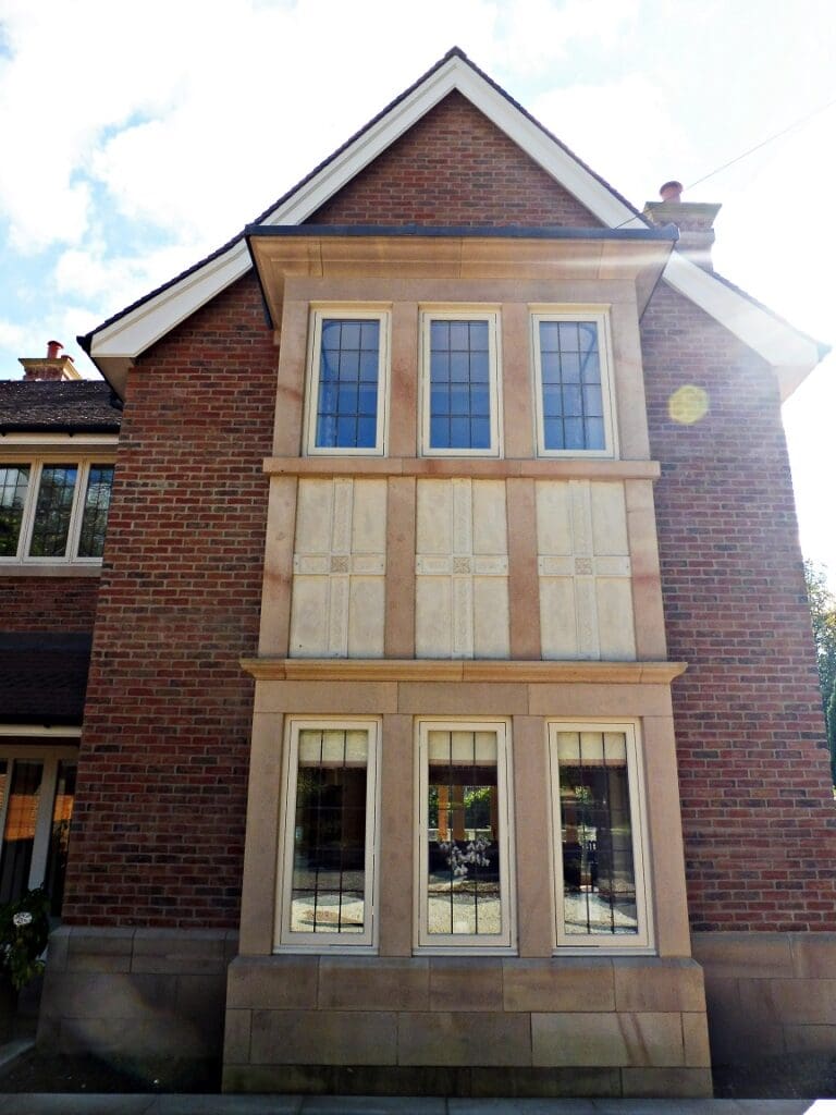 Two-storey square bay featuring stone mullions and Hardwick casement windows with square leaded glazing, painted in a pale cream finish.