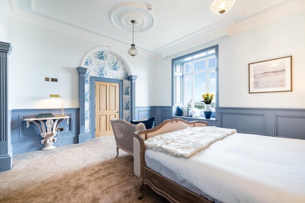 Richmond-style casement window in luxury bedroom, Riber Castle
A stylish, light-filled bedroom in Riber Castle, Matlock, Derbyshire, featuring elegant blue panelling and a Gowercroft timber casement window. The sashless window set into a deep reveal creates a peaceful window seat overlooking the Derbyshire Dales. Interiors include heritage mouldings, a crystal chandelier, and a soft, neutral palette. Image courtesy of Dales and Peaks.