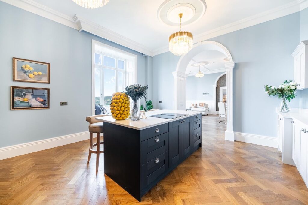 Richmond casement window in blue kitchen interior, Riber Castle
A high-ceilinged kitchen inside Riber Castle, Matlock, Derbyshire, featuring crisp blue walls, detailed cornicing, a statement chandelier and a black kitchen island. The Gowercroft Richmond casement window is set in a deep blue-painted reveal and offers scenic views over the countryside. Image courtesy of Dales and Peaks.