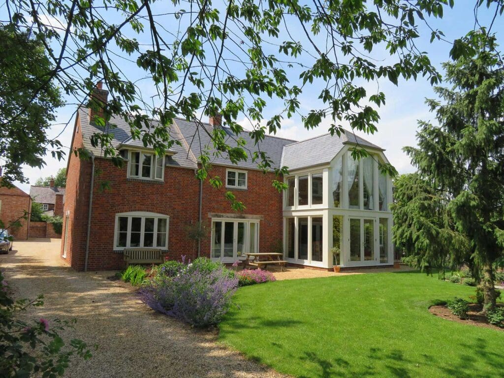 Two-storey red brick new build in Lutterworth with Gowercroft’s cream-painted timber flush casement windows and doors, including a large glazed extension framed in timber, set in a landscaped garden.