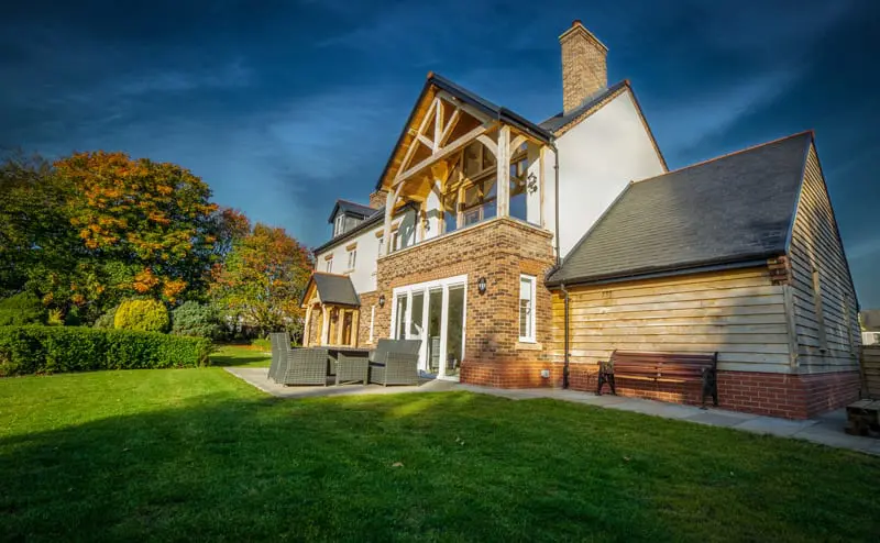 Rear elevation of a large countryside home in Hartlepool featuring Gowercroft timber casement windows, painted French doors, and a two-storey oak-framed glazed gable overlooking a landscaped garden.