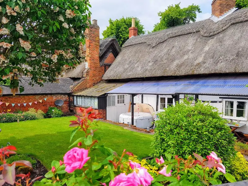 Richmond casement windows with heritage-style sealed units installed in a thatched cottage at Repton School, Derbyshire, surrounded by a vibrant garden and traditional red brickwork.
