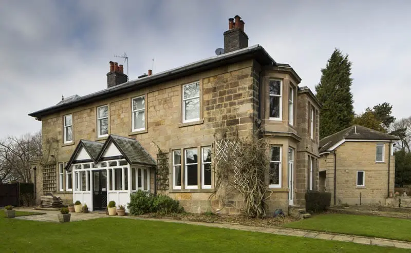 Large traditional stone house in Quarndon, Derbyshire, featuring Gowercroft double-glazed timber sliding sash windows with a white-painted finish, including a prominent bay window and glazed porch extension.