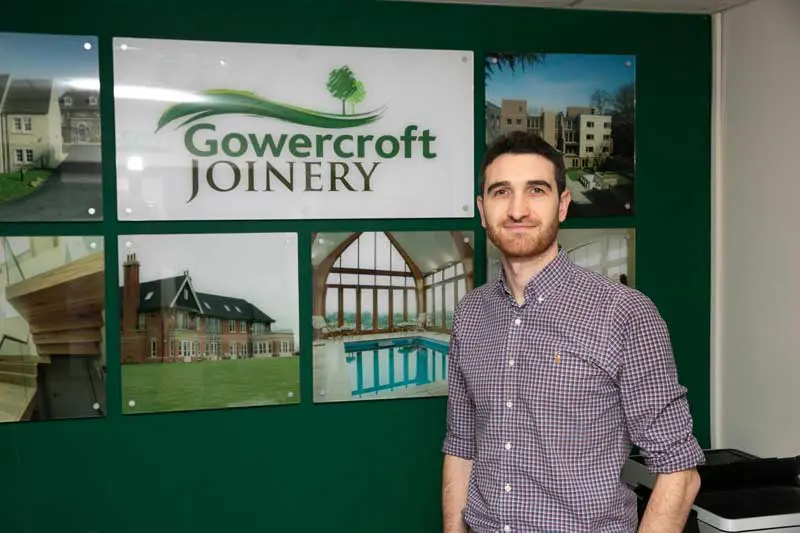Andrew Madge stands in front of Green wall with Gowercroft Joinery logo and images of completed projects