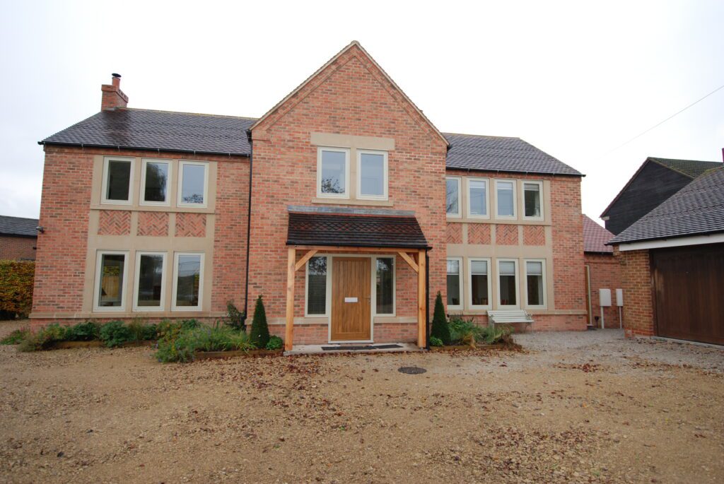 Front elevation of a large red brick home featuring evenly spaced Hardwick flush casement windows, alongside a centrally placed Melbourne front door stained in Walnut. The driveway and small planting beds frame the neat exterior.