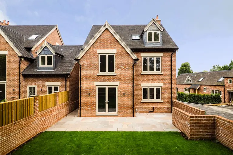 Rear elevation of a new build red-brick property in Melbourne, Derbyshire, featuring Gowercroft’s timber flush casement windows and double doors, with stone lintels and a neatly landscaped patio and lawn.