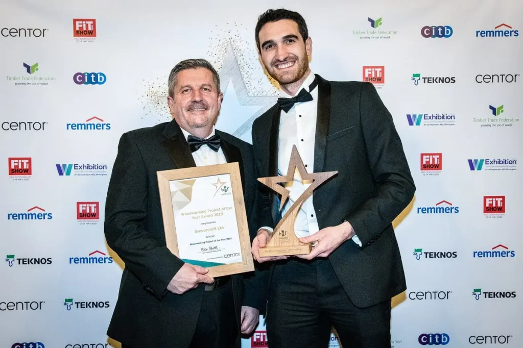 Gowercroft Employees wear formal suits and hold trophy and certificate for Woodworking Project of the Year