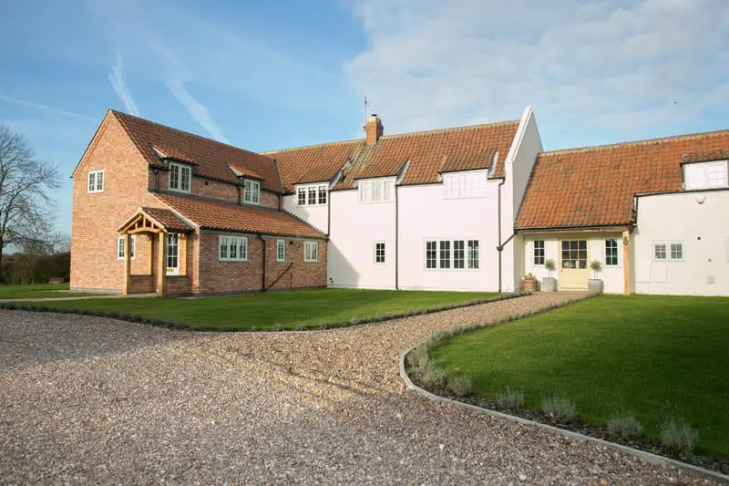Wide-angle view of White Cottage in Nottinghamshire, showing the red brick and white-rendered exterior with Gowercroft’s timber flush casement windows and a clay tiled roof, set against a clear blue sky.