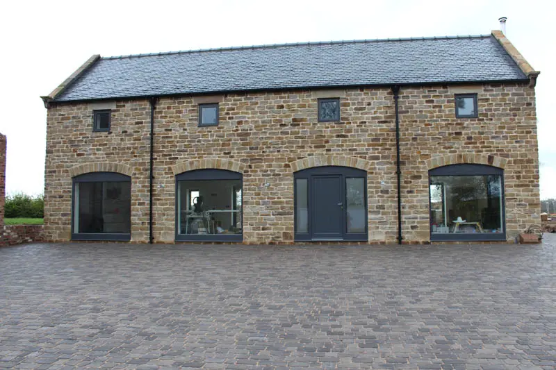 Front elevation of a traditional stone barn conversion in Chesterfield featuring large arched windows and a central entrance door in a dark grey finish, all supplied by Gowercroft Joinery.