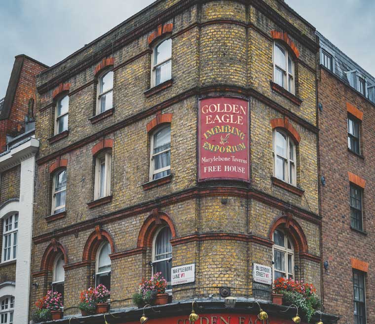 Historic brick building featuring traditional sash windows with segmental arch detailing, located at the corner of Marylebone Lane and Buxbridge Street in London, with a vintage "Golden Eagle Imbibing Emporium" pub sign.