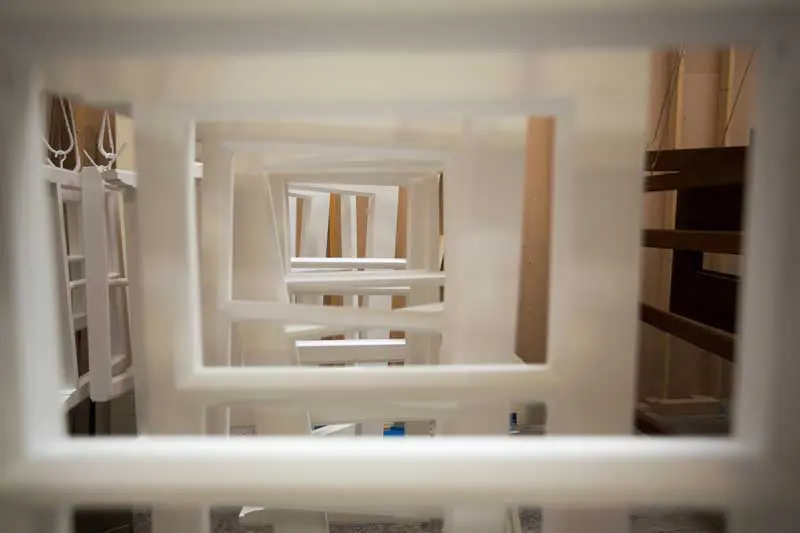 View through multiple white-painted timber sash window frames hanging in a drying area, showing uniform craftsmanship and alignment in a workshop setting.