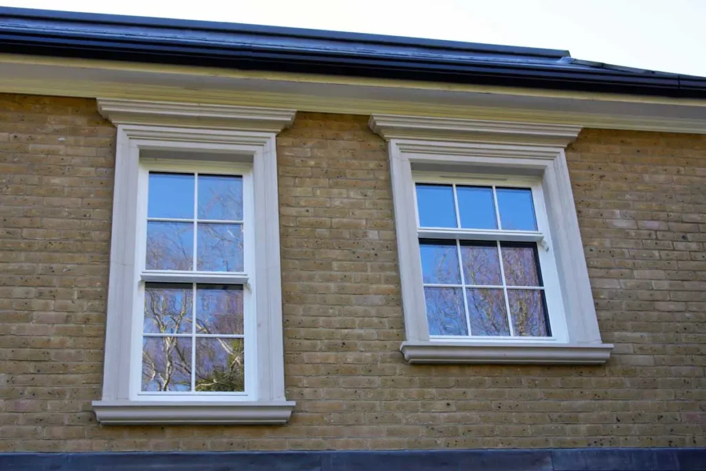 Close-up view of two double-glazed white timber sash windows set in a traditional yellow brick building with decorative stone surrounds and deep moulded lintels.