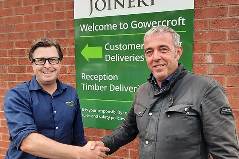 Two men shake hands in front of Gowercroft Joiner Sign