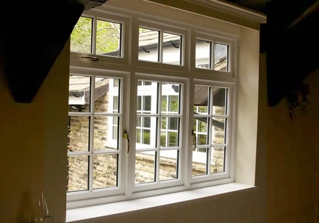 Interior view of a timber flush casement window with multiple glazed panes, showing traditional detailing and brass handles, looking out onto a stone-built courtyard.