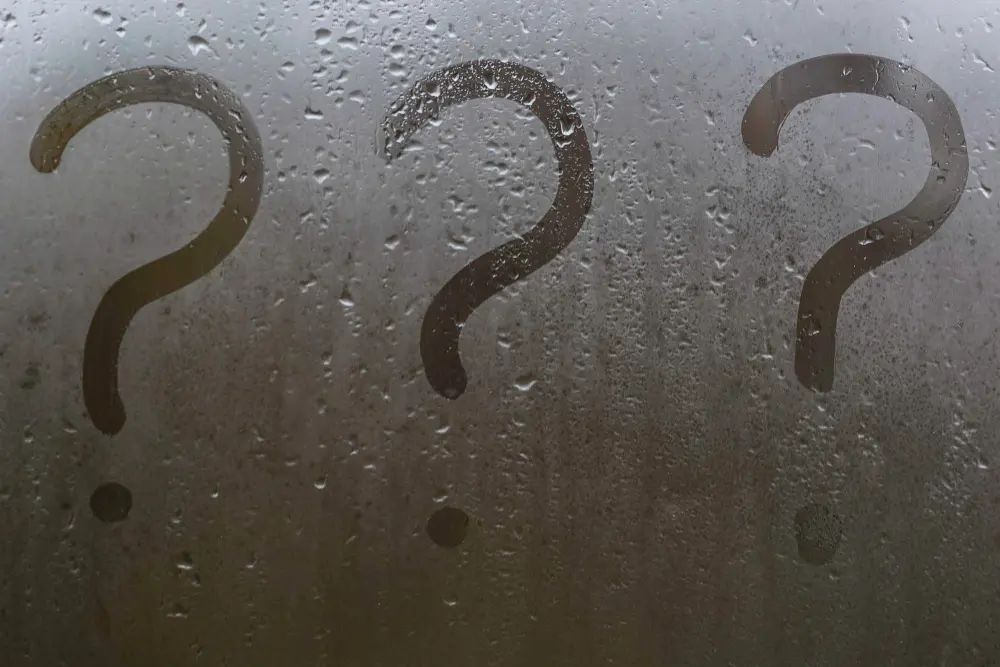Condensation-covered window with three question marks drawn in the mist, representing uncertainty or queries about glazing and insulation options.