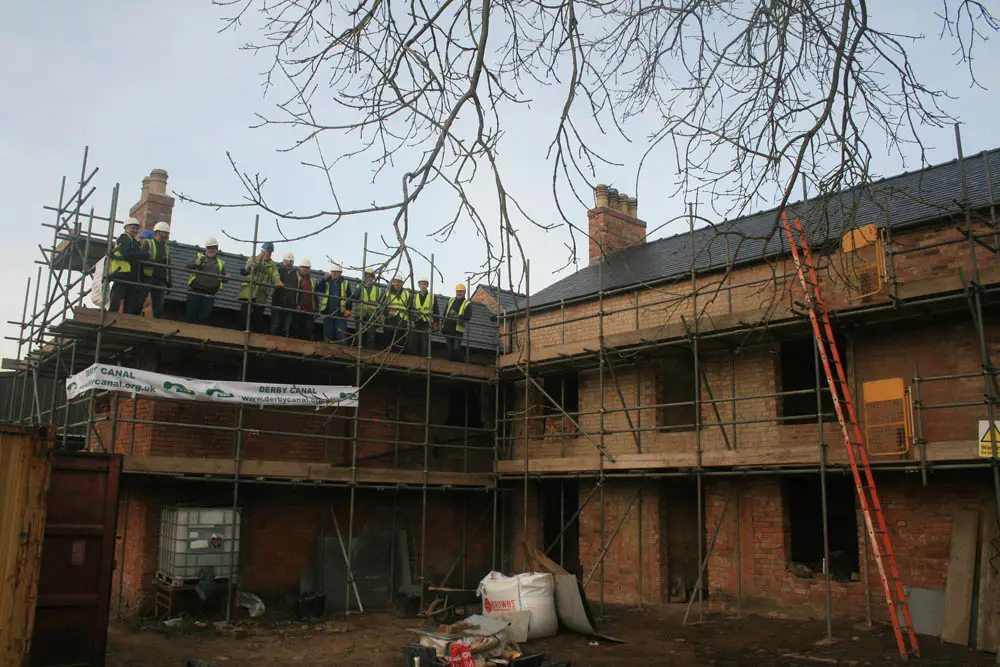 Canal Side Cottages: long shot of the cottages in a state of disrepair before restoration with the team lined up on the scaffold