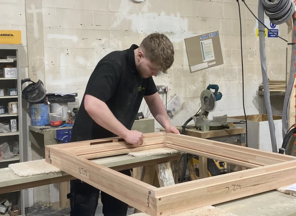 Gowercroft apprentice sanding a timber window frame in the workshop as part of his woodworking training.