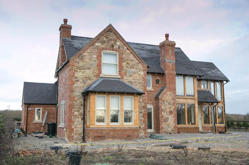 A large stone and brick-built home featuring traditional timber sash windows installed throughout the property.