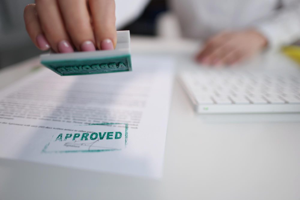 A close-up of a person stamping a document with the word "APPROVED" in green ink, symbolising successful planning permission or official authorisation.