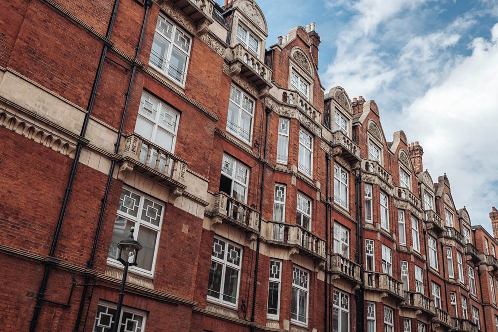 A row of historic red brick buildings with white-framed sash windows and decorative stone balconies, representing typical Grade II listed architecture in the UK.