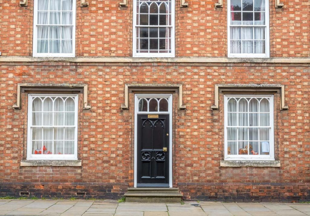 Front view of a traditional red brick listed building with arched timber sash windows and a black period-style front door, showcasing historic architectural features
