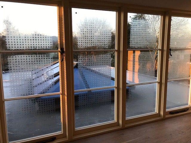 Close-up of vacuum glazed windows showing temporary visible evacuation dots used during manufacturing, with a scenic view outside at sunrise.