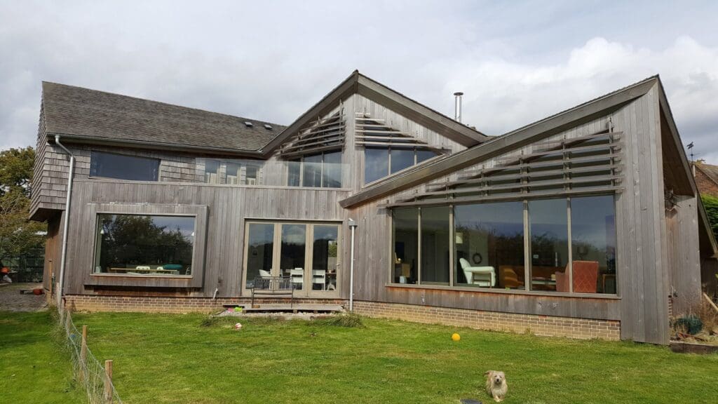 A striking modern home with sharp angular rooflines and extensive timber cladding, featuring large glass windows and clean architectural lines. The exterior showcases the natural weathering of Accoya wood, known for its durability, stability, and sustainable credentials.