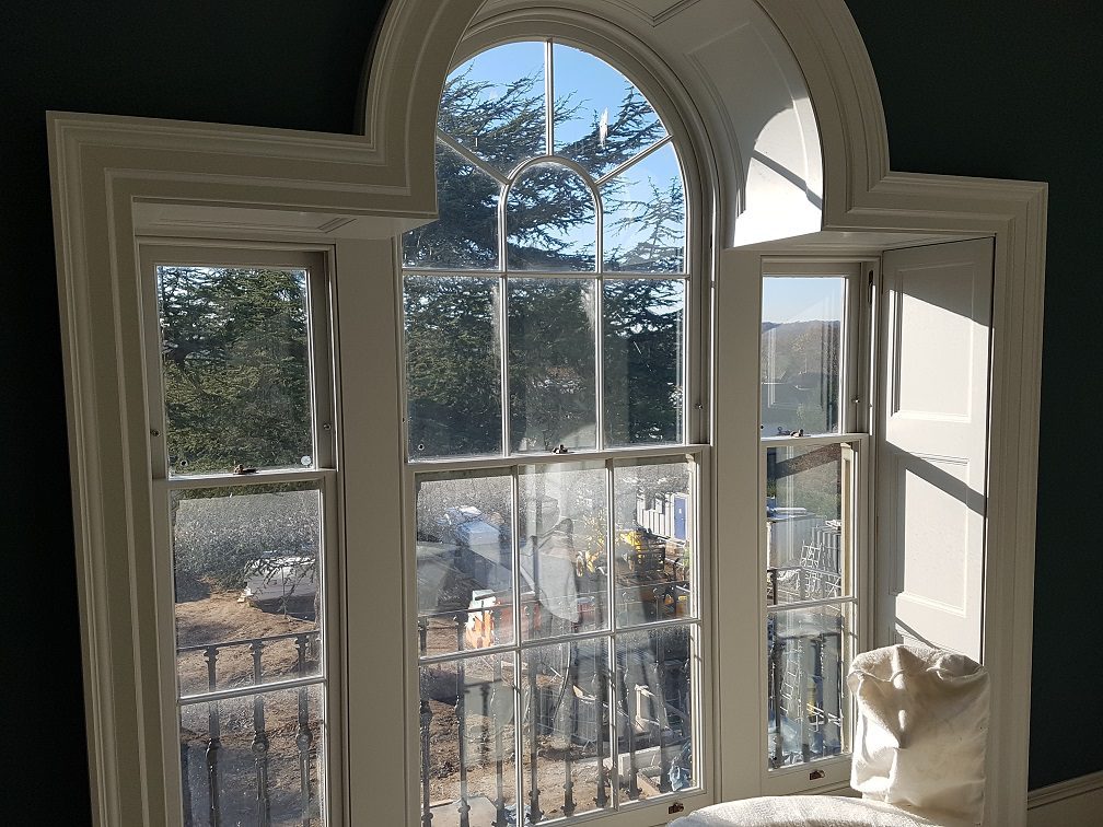 Internal view of three curved-top Palladian-style Winston sliding sash windows with Georgian glazing bars. The windows are framed with custom shutter boxes and painted to match the interior, showcasing a traditional yet functional design that allows for natural light while preserving the building's historic character.