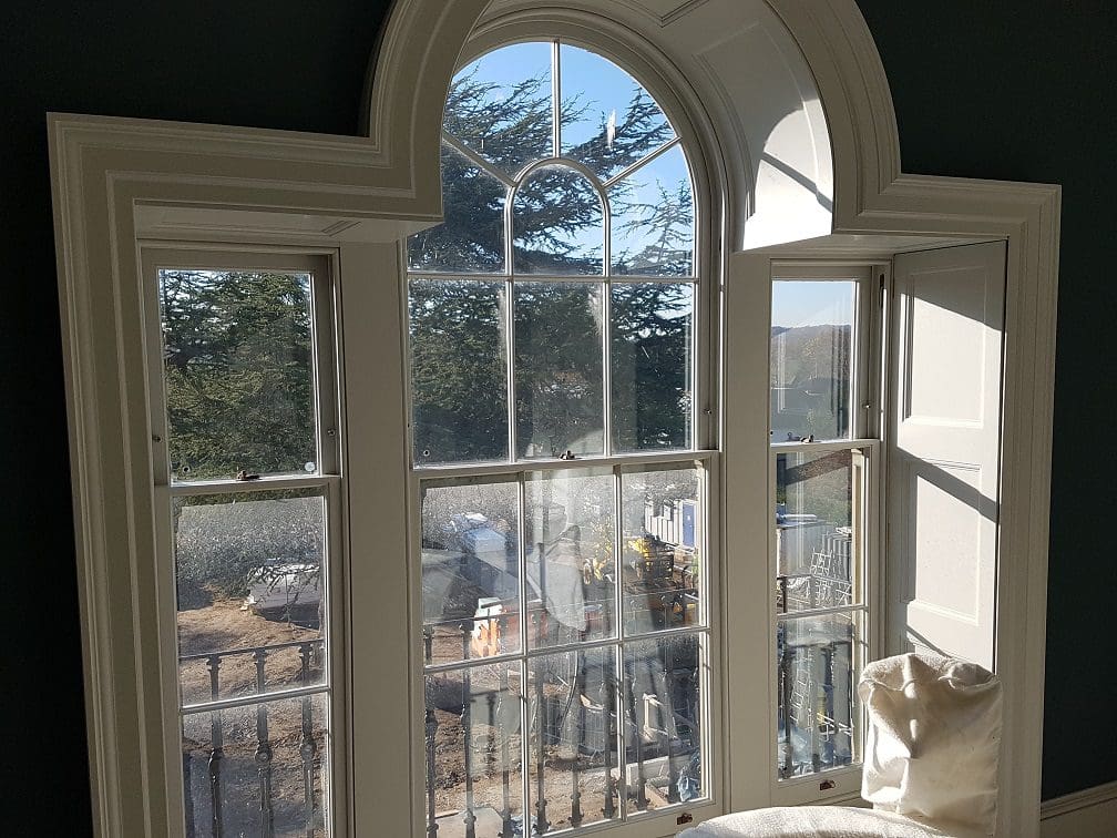 Internal view of three curved-top Palladian-style Winston sliding sash windows with Georgian glazing bars. The windows are framed with custom shutter boxes and painted to match the interior, showcasing a traditional yet functional design that allows for natural light while preserving the building's historic character.