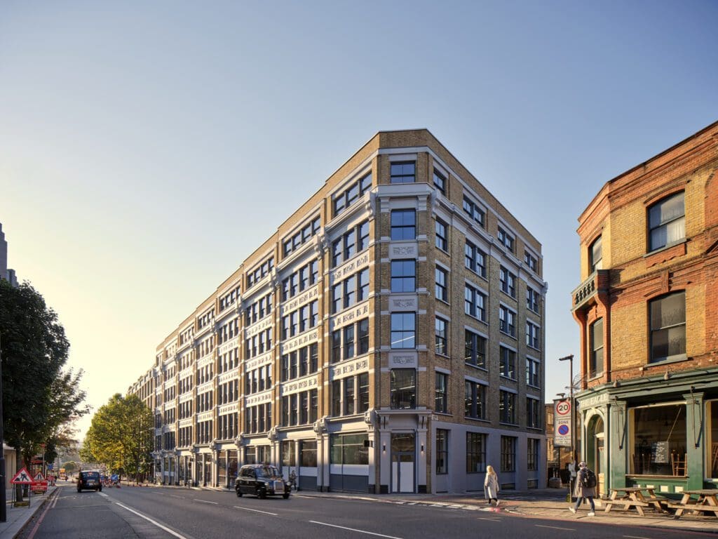 Exterior of The Waterman Building, Farringdon, London – A large, six-storey Victorian warehouse building with a grand, symmetrical façade in warm yellow brick. Rows of black-painted timber sash windows contrast with ornate white stone detailing. The corner section features decorative pilasters and a rounded edge, standing proudly on a busy London street in the Borough of Islington.