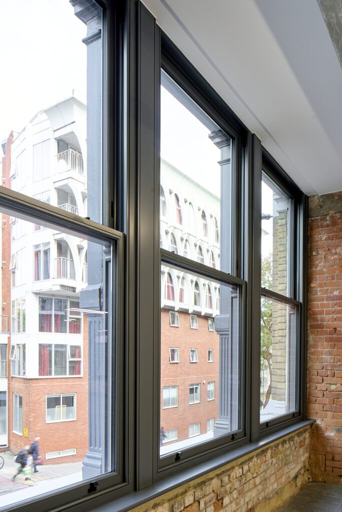 Close-up of Chatsworth sliding sash windows at The Waterman Building, Farringdon – A detailed look at the black-painted timber sash windows set within the brickwork. The delicate glazing bars divide the glass panes into a traditional pattern, maintaining the heritage aesthetic while offering modern performance.