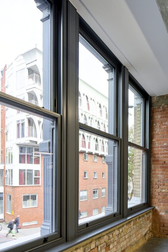 Close-up of Chatsworth sliding sash windows at The Waterman Building, Farringdon – A detailed look at the black-painted timber sash windows set within the brickwork. The delicate glazing bars divide the glass panes into a traditional pattern, maintaining the heritage aesthetic while offering modern performance.