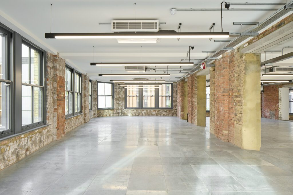 Industrial-style office with exposed brick and sash windows – The Waterman Building, Farringdon, London
A heritage-meets-modern office interior featuring tall Chatsworth sliding sash windows, exposed brick columns, and sleek black pendant lighting. The combination of raw textures and contemporary fixtures highlights the building’s conservation-led renovation.