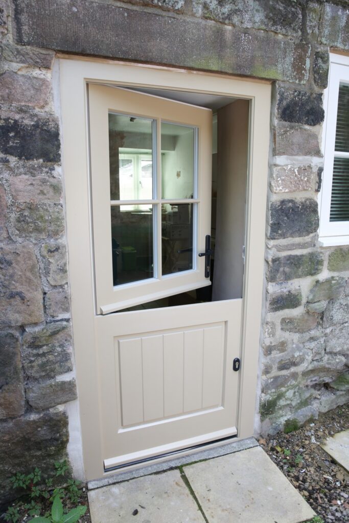 Cream-coloured Melbourne Stable Door set within a traditional stone cottage. The top half is open, allowing fresh air inside while keeping the lower section closed for security and practicality. The four-pane glazed window adds charm and natural light, while the timber construction blends seamlessly with the rustic surroundings. Perfect for farmhouses, cottages, and country homes looking for a classic yet functional entrance