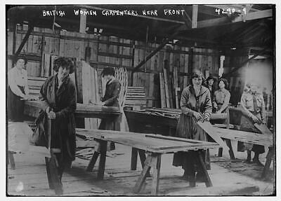 Black-and-white historical photograph showing a group of women carpenters working at large wooden benches in a workshop during World War I. Three women in the foreground are holding hammers and smiling, while others work in the background. The women are dressed in work overalls and surrounded by timber boards. Believed to be part of the W.G. Tarrant team in Calais.