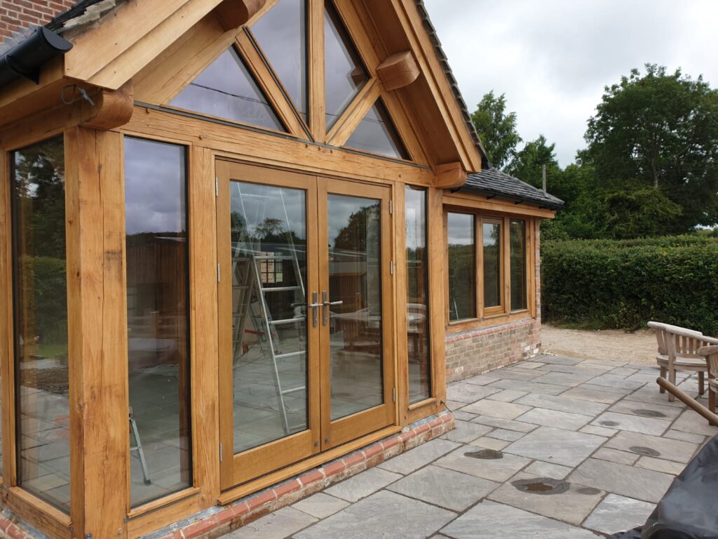 A timber-framed garden room extension featuring large glazed panels and double doors in a warm oak finish, showcasing how high-quality timber in UK housing enhances character, natural light and countryside views.