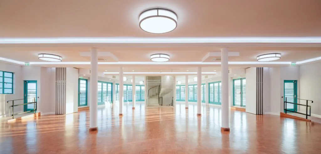 Internal Panorama of Curved Tutbury Bi-Fold Doors and Melbourne French Doors A wide-angle interior view of Saltdean Lido’s event space, showcasing the curved Tutbury Bi-Fold Doors and Melbourne French Doors in turquoise. Natural light floods the room, highlighting the restored parquet flooring and period-accurate lighting.