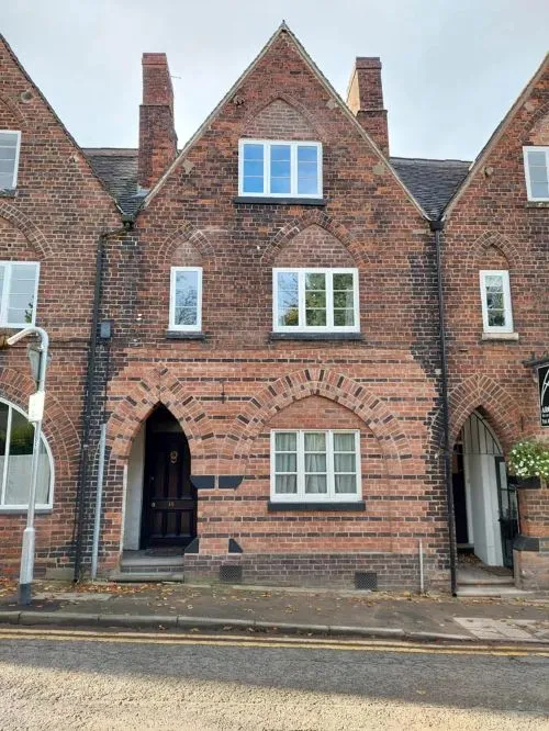 Red brick heritage building with pale timber casement windows, decorative brick arches and arched entrances facing a quiet street.