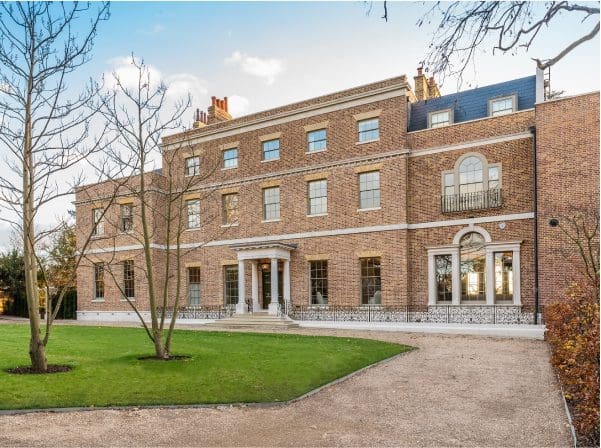 Georgian brick building with sash windows, arched doorway, columned entrance and gravel driveway beside a landscaped lawn.